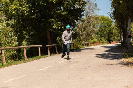 Young Caucasian Latino mix roller skater in a park, wearing a black mask for prevention of pandemic...