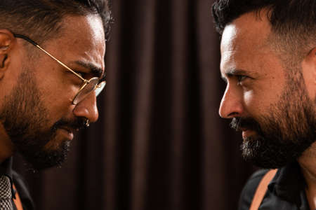 A white Caucasian man and a black African-American man come face to face with a black backdrop, theater. staging, they go in suspenders and hipster style. one wears glasses and both have beards.の写真素材