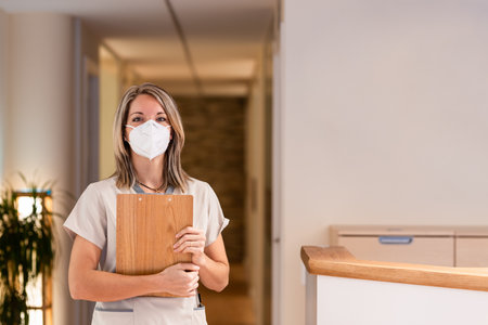 woman receptionist holding folder with documents and with mask in hospitalの写真素材