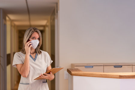nurse answers the phone holding a folder and a protective mask in the hospitalの写真素材