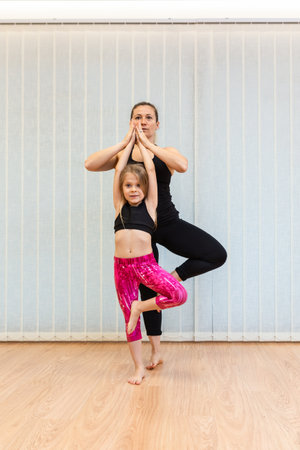 the mother yoga instructor and the daughter perform the tree positionの写真素材