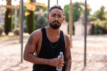 african american athlete boy with tattoo drinks water from a bottle in a park.