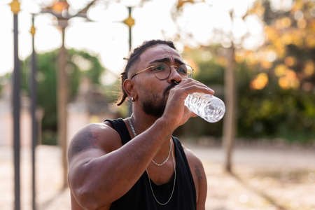 african american athlete boy with tattoo drinks water from a bottle in a park.の写真素材
