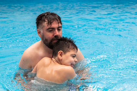 child with disability laughs and plays in his fathers arms in a swimming poolの写真素材