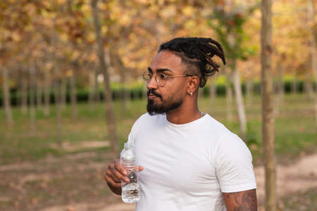 african american athlete boy with tattoo drinks water from a bottle in a park.の写真素材