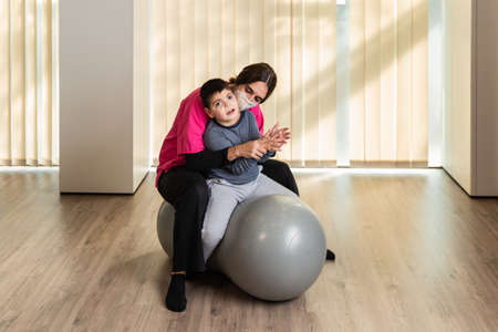 disabled child and physiotherapist on top of a Peanut Gym Ball doing balance exercises. pandemic mask protectionの写真素材