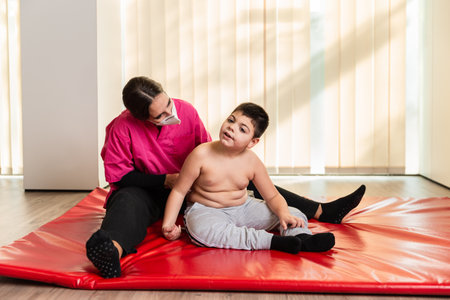 disabled child and physiotherapist on a red gymnastic mat doing exercises. pandemic mask protectionの写真素材