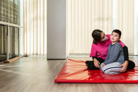 disabled child and physiotherapist on a red gymnastic mat doing exercises. pandemic mask protectionの写真素材