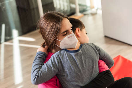 child with disabilities is hugged by physiotherapist wearing protective maskの写真素材