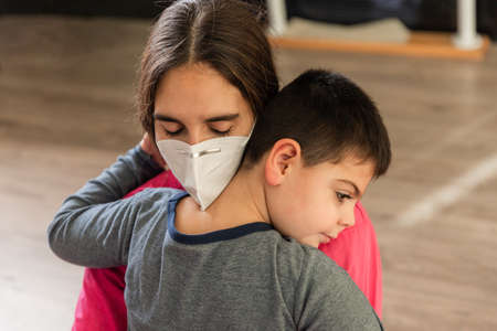 child with disabilities is hugged by physiotherapist wearing protective maskの写真素材