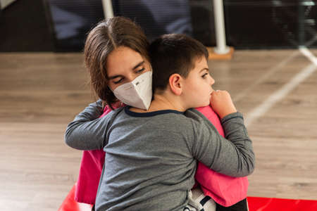 child with disabilities is hugged by physiotherapist wearing protective maskの写真素材