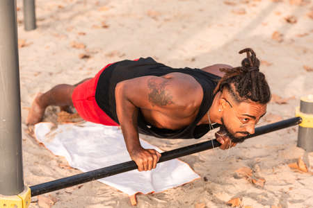 african american boy does push-up exercises on a barbell in a calisthenics park.の写真素材