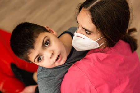child with disabilities is hugged by physiotherapist wearing protective maskの写真素材