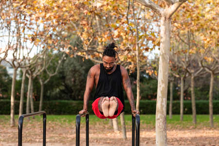 african american athlete boy does calisthenics fitness exercises on bars in parkの写真素材