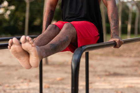 african american athlete boy does calisthenics fitness exercises on bars in park