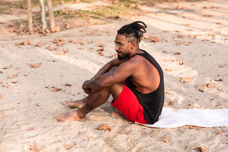 sports guy is sitting on a towel in a park, usually sand. he is african americanの写真素材