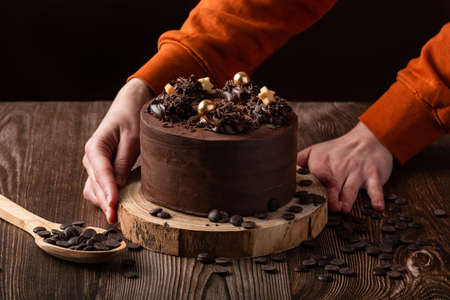 front view of chocolate cake, chocolate chips, spoon wooden and 2 hands
