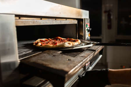 freshly made pepperoni pizza, coming out of the oven of a pizzeria with shovel.の写真素材