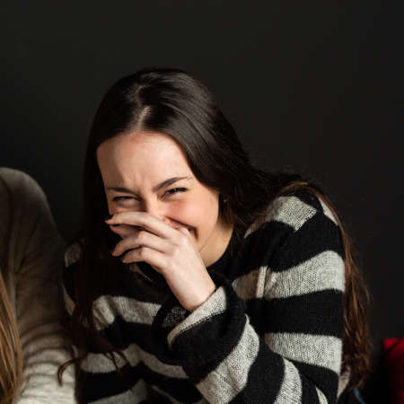 beautiful caucasian girl covers her face with her hands while laughing.