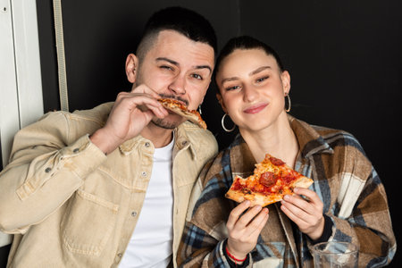 a couple looks at the camera while eating a slice of pizza