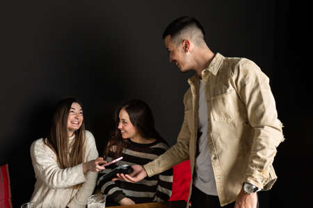 two girls pay the waiter with a POS with their cell phones