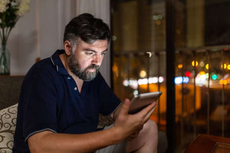 bearded man on sofa uses digital tablet in dining room overnightの写真素材
