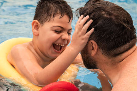 disabled boy with a float laughs as he plays and swims in a pool with his father