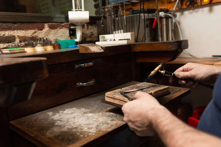 goldsmith jeweler heats a piece of silver with a gas torch to make a ring.