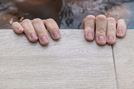 the two hands of a Caucasian person holding on to the edge of the swimming poolの写真素材