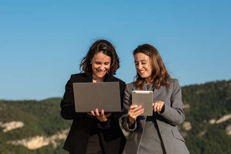 Cheerful businesswomen using laptop and tablet in natureの写真素材