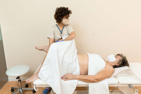Physiotherapist performing leg massage to mature woman with towelsの写真素材