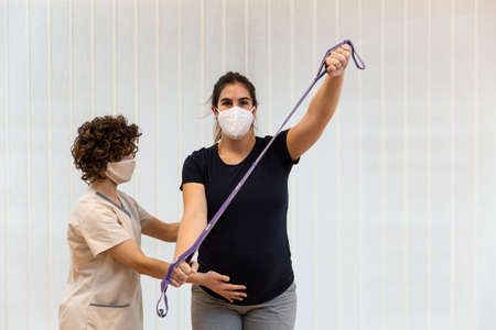 A pregnant woman exercising with an elastic band with help of physiotherapistの写真素材