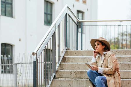 An adult woman sitting on the steps of the stairs of a building taking notesの写真素材