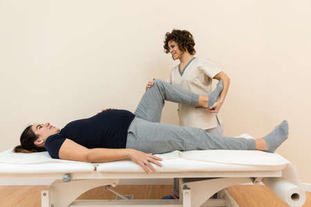 A pregnant woman lying on a massage table while a physiotherapist massages her legs at a health...