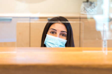 Woman wearing a face mask and sitting behind desk while working at a reception of a spa or health center.の写真素材