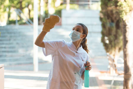 Young woman cleaning windows of clinic on outsideの写真素材