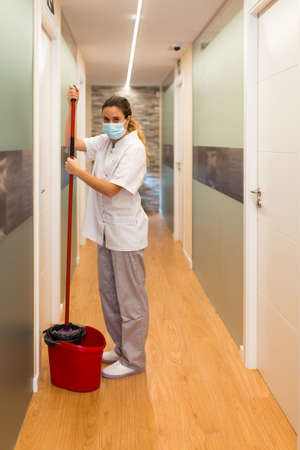 Woman standing holding mop in a bucket looking at camera in hallway of physiotherapy centreの写真素材