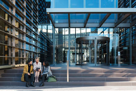 Professional coworkers discussing new projects while sitting on the stairs outside the office building.の写真素材