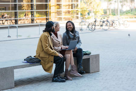 Business people using a laptop together while discussing new business projects sitting on a bench on...