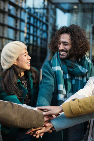 Cheerful diverse coworkers stacking hands together with colleagues on city streetの写真素材