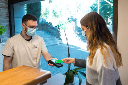 Receptionist holding credit card reader device receiving contactless payment from patient