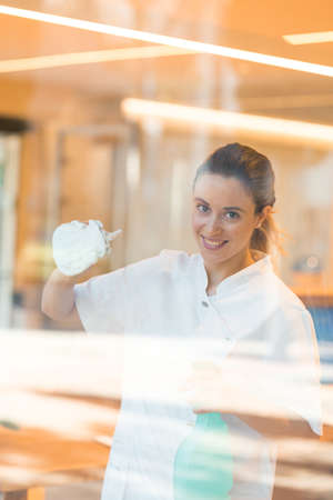 Smiling woman cleaning windows at modern hospitalの写真素材