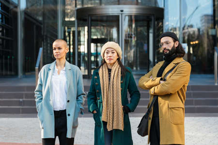 Three professional business people posing together in front of the office building in the financial...