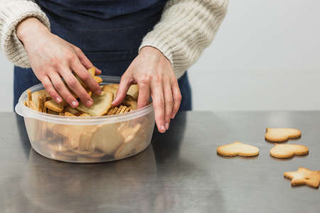 Woman putting freshly baked cookies in plastic bowl