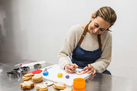 Cheerful pastry chef writing on decorated cookies in pastry shopの写真素材