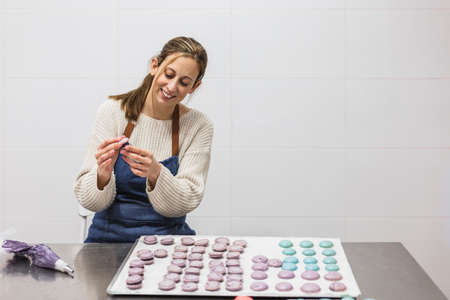 Cheerful woman making macaroons in bakery in bakehouseの写真素材