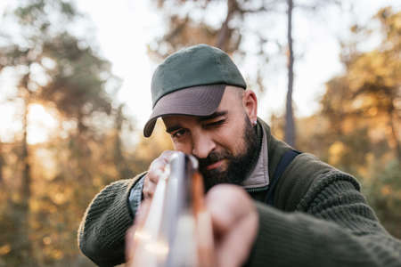 Bearded man with rifle hunting in sunny woods