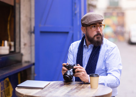 Man checking the images on the camera while relaxing sitting in a coffee shop outdoors.の写真素材