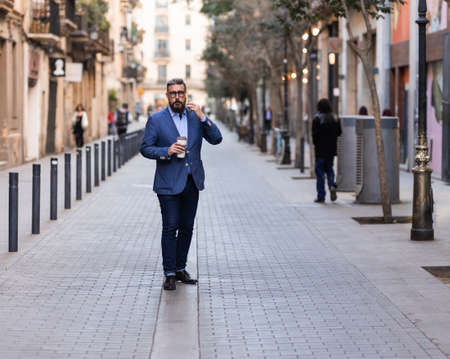 Businessman standing on the city talking on phone and holding coffee cupの写真素材
