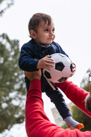 Father holding his little son up in the air with a soccer ball while playing together outdoors in the park.の写真素材